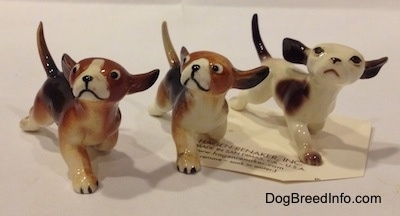 The front right side of three figurines of running dogs in different color variations. The figurines are looking up and to the left.