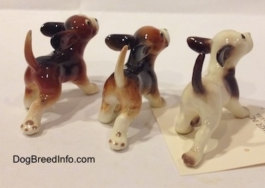 The back right side of three running dog figurines in different color variations. The figurines tails are arched up in the air.