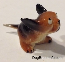 The front right side of a miniature figurine of a running puppy. The figurine has black tipped nails.