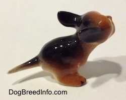 The back right side of a miniature running puppy figurine. The figurine is glossy.