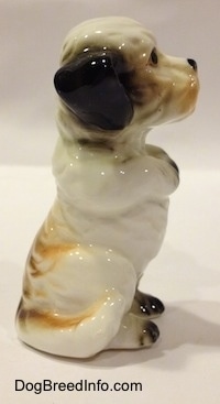 The right side of a figurine of a bone china white with black Peek-A-Poo in a begging pose. The figurine has a long tail that runs along the side of its leg.