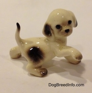 The right side of a white brown spotted Hound dog with its paw in the air. The figurine has black circles for eyes and a nose.