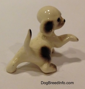 The back right side of a Hound dog figurine with a paw in the air. The figurine also has its long tail in the air and at the tip is a brown spot.