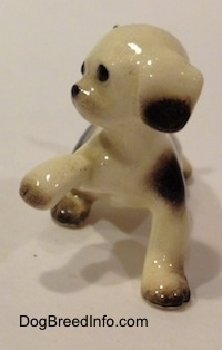 The front of a brown spotted Hound dog figurine with a paw in the air. The figurine has brown at the bottom of its ears.