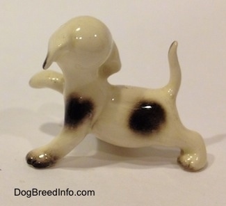 The left side of a brown spotted Hound figurine. The figurine has a brown spot on its arm and it has brown tipped paws.