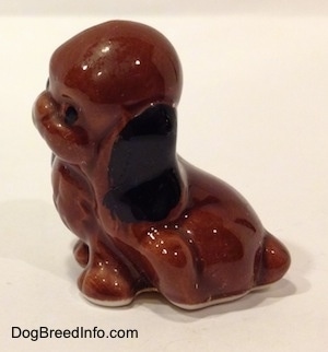 The left side of a figurine of a brown with black mixed dog in a sitting position. The figurine is very glossy.
