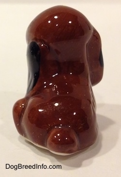 The back of a brown with black figurine of a mixed dog in a sitting position. The figurine has a short brown tail.