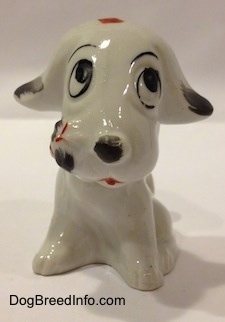 A white with black bone china mixed breed dog figurine that is in a sitting pose.