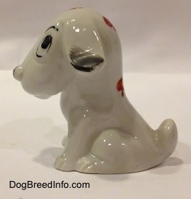 The left side of a bone china white with black mixed breed dog figurine that is in a sitting pose. The bottoms of the figurines ears are black.