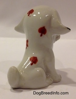 The back right side of a white with black figurine that is in a sitting position. The figurine has four red spades on its back.