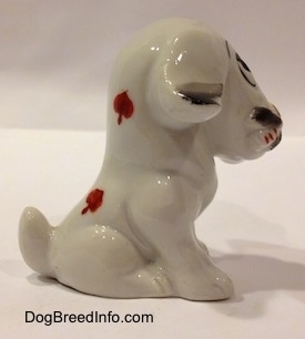 The right side of a white with black figurine of a sitting mixed breed dog. The figurine has a shirt tail.