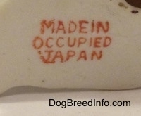 Close up - A stamp on the underside of a mixed breed dog figurine that reads 'Made in Occupied Japan'.