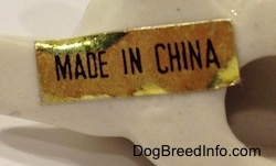 Close up - The underside of a bone chine puppy lying down figurine and there is a gold sticker that reads 'Made In China'.