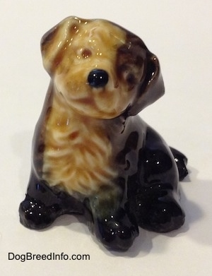 A ceramic black, brown and tan puppy figurine. The figurine does not have eyes painted on. It looks like the figurine has a smile on.