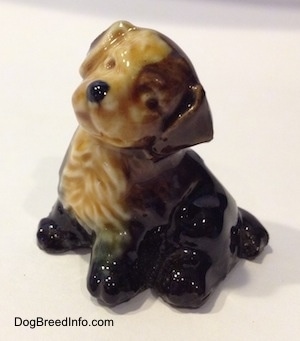 The left side of a ceramic black, brown and tan puppy figurine. It is looking to the left and the head of the figurine is tilted to the right. It has a black nose and a cute face.