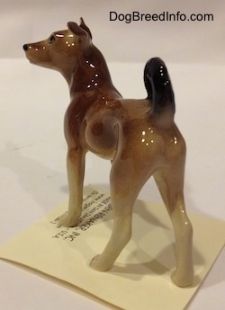 The back left side of a mixed breed dog figurine. The figurine has long legs.