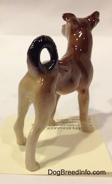 The back right side of a figurine of a mixed breed dog figurine. The figurine has its ears perked up.