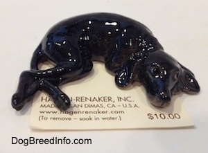 A black dog with grey highlights figurine is in a sleeping pose.