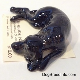 The left side of a black dog with grey highlights that is in a sleeping pose figurine. The figurine has long legs.