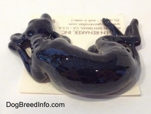 The back of a black dog with grey highlights figurine that is in a sleeping pose. The figurine is glossy.