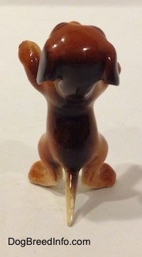 The back of a dog standing figurine that is standing on its hind legs and in a begging pose. The figurine has a long skinny tail.