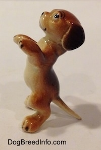 The left side of a figurine of a dog that is standing on its hind legs in a begging pose. The figurine has a smile on its face.