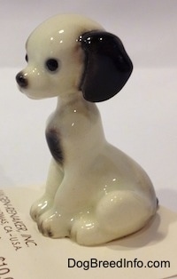 The left side of a figurine of a white with black sitting puppy. The puppy has balck circles for eyes.