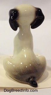 The back of a figurine of a white with black sitting puppy figurine. The figurine has a short black tail.