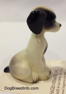 The right side of a white with black sitting puppy figurine. The figurine has a black ears.
