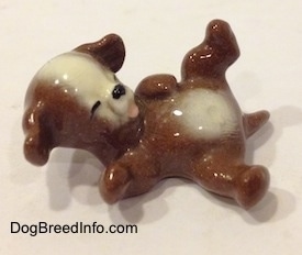 A figurine of a brown with white dog that is laying on its back.