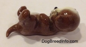 The right side of a brown with white dog figurine that is laying on its back. The eyes of the figurine are painted closed.