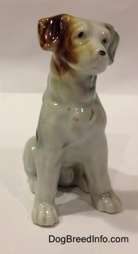 The front right side of a figurine of a bone china brown, white and black mixed breed dog in a sitting pose. The figurine has black circles for eyes.