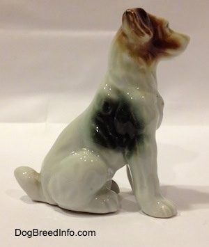 The right side of a bone china mixed breed dog in a sitting pose. The figurine has a spot on its side.