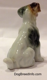 The back right side of a bone china figurine of a mixed breed dog in a sitting pose. The figurine has a brown ear and a black ear.