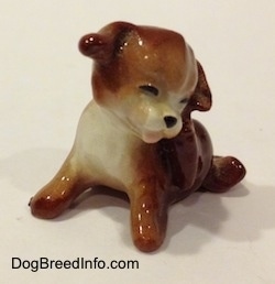 The front left side of a figurine of a brown with white puppy. The puppy has its mouth painted open.