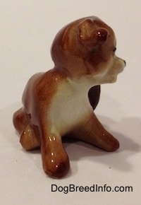 The front left side of a brown and white puppy figurine that is scratching its neck. The figurines ears are hard to differentiate from its body.