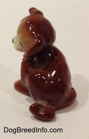 The back of a brown and white figurine of a puppy scratching its neck. The figurine has a short curled taill.