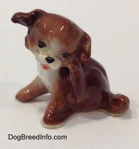 The left side of a brown and white figurine of a puppy scratching its neck. The figurine has black circles for eyes.