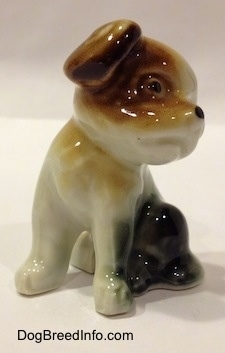 The front left side of a figurine of a brown, black and white dog that is sitting. The figurine has detailed black circles for eyes.
