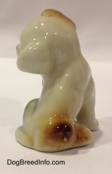 The back side of a figurine of a brown, black and white dog sitting. The figurine has a small tail.