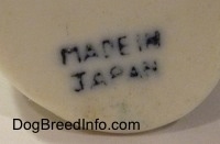 Close up - The underside of a figurine of a dog sitting. The words 'Made In Japan' are stamped on the bottom of the figurine.