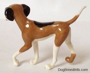 The left side of a figurine of a tri-color Papa Dog figurine. The tail of the figurine is long and skinny.
