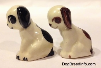 The left side of two dog figurines in a sitting position. The figurines have large spots on there backs.