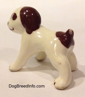 The back left side of a white with brown dog standing figurine. The figurine has large brown eyes.