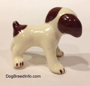 The right side of a white with brown dog standing figurine. The figurine has brown ears.