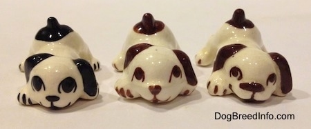 Three figurines of a puppy in a play bow pose that are color variations. The figurines have basic features.