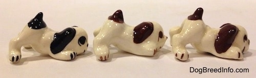The right side of three figurines that are of a puppy in a play bow pose and they are color variations of each other.