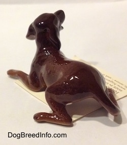 The back left side of a figurine of a brown playful dog. The figurine has a long tail.
