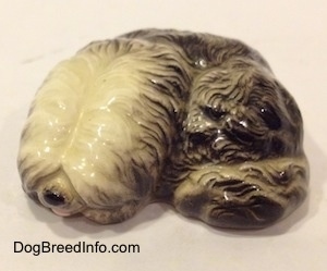 A miniature black with white Old English Sheepdog figurine that is in a lying down pose.