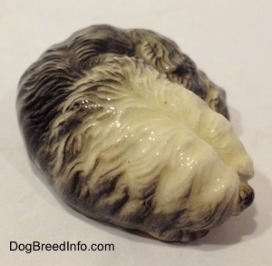 A figurine of a black with white miniature Old English Sheepdog that is in a lying down pose. The figurine has a great hair details.